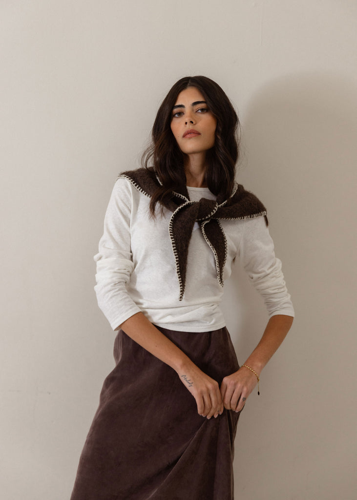 A woman modeling a white long-sleeve top with a dark brown knit collar featuring white trim, paired with a dark brown skirt, against a plain beige wall.