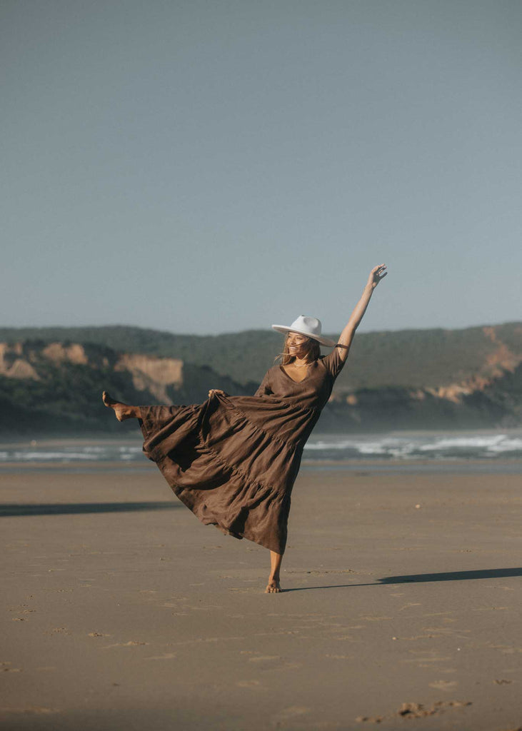 The Elwood Maxi dress in Mocha on the beach in Australia during golden hour. Our model shows off the beautiful tiers and volume of the dress with a big smile on her face.