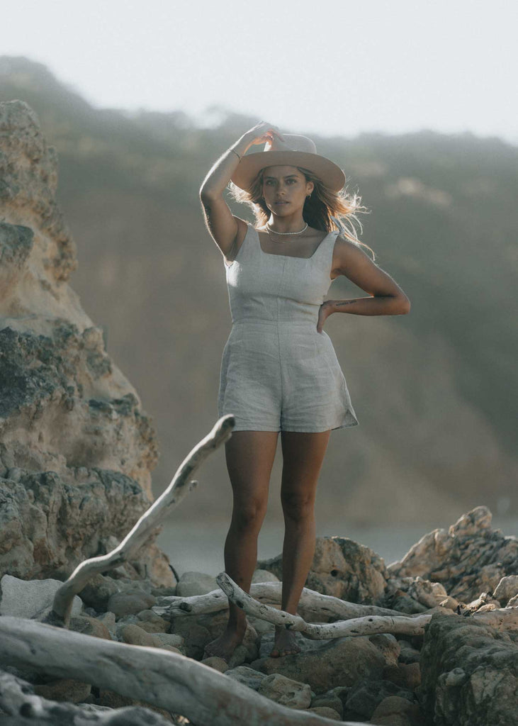 The Mallee Romper at golden hour on the beach in Australia. This linen romper has adjustable tie-up straps and a square neckline. The shorts have slits up the side and is an effortlessly chic outfit ethically made in Vancouver.